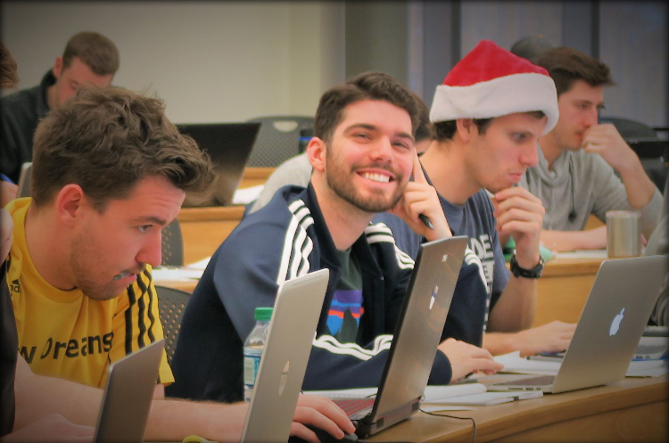 Austin, in class, sitting with classmates and using his laptop.